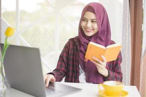 mulher muçulmana com hijab está trabalhando com computador portátil na cafeteria foto