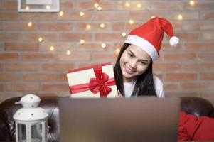 jovem sorridente usando chapéu de papai noel vermelho fazendo videochamada na rede social com a família e amigos no dia de natal.