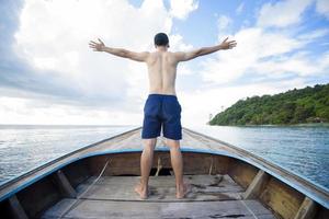 vista do homem em traje de banho desfrutando no tradicional barco tailandês de cauda longa sobre a bela montanha e oceano, ilhas phi phi, tailândia foto