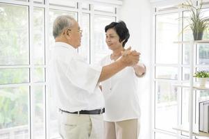 alegre casal de aposentados asiáticos sênior está dançando e curtindo a música na sala de estar em casa, conceito de saúde foto