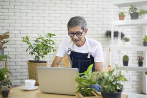 feliz homem aposentado asiático sênior com laptop está relaxando e desfrutando de atividades de lazer no jardim em casa. foto