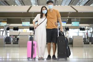 um casal asiático está usando máscara protetora no aeroporto internacional, viaja sob pandemia de covid-19, viagens de segurança, protocolo de distanciamento social, novo conceito de viagem normal. foto