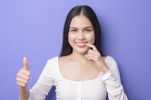 jovem mulher bonita sorridente está mostrando e apontando seus dentes brancos retos saudáveis sobre o estúdio de fundo roxo foto