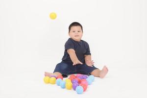 retrato de menino adorável bonitinho está sentado e jogando bolas coloridas no estúdio de fundo branco foto