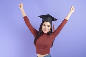 retrato de mulher jovem estudante universitário com chapéu de formatura em fundo violeta
