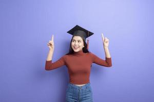 retrato de mulher jovem estudante universitário com chapéu de formatura em fundo violeta