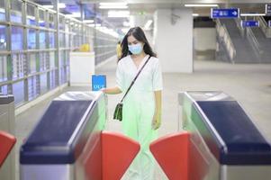 uma jovem usando máscara protetora no metrô está usando álcool para lavar as mãos, viajar sob pandemia covid-19, viagens de segurança, protocolo de distanciamento social, novo conceito de viagem normal foto