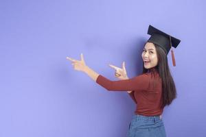 retrato de mulher jovem estudante universitário com chapéu de formatura em fundo violeta foto