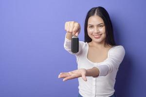 jovem e bela mulher sorridente está segurando a chave do carro sobre estúdio de fundo roxo isolado foto