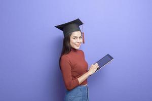 retrato de mulher jovem estudante universitário com chapéu de formatura em fundo violeta foto