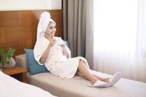 uma mulher relaxada vestindo roupão branco e toalha tomando um café da manhã foto