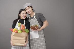 casal feliz está segurando legumes na sacola de compras em fundo cinza de estúdio foto