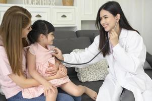 uma médica segurando estetoscópio está examinando uma garota feliz no hospital com sua mãe, conceito médico foto