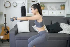 mulher jovem e bonita no sportswear exercitando com halteres em casa foto