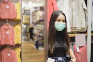 mulher com máscara facial está comprando roupas no shopping foto