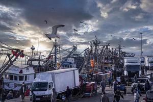 as pessoas andam pelo mercado ao lado de caminhões e barcos de pesca na marina foto