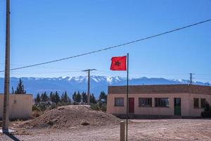 bandeira de Marrocos flutuando no vento contra montanhas cobertas de neve ao fundo foto