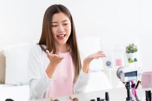 sorridente jovem influenciadora de beleza asiática gravando vídeo com câmera em casa foto