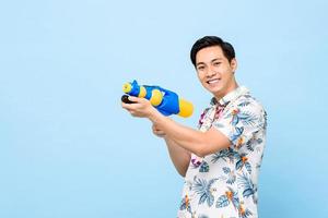 sorrindo bonito homem asiático brincando com pistola de água durante o festival songkran na tailândia e sudeste da ásia foto