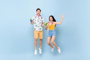 jovem casal asiático em roupas de verão com armas de água pulando em fundo azul de estúdio para festival songkran na tailândia e sudeste asiático foto