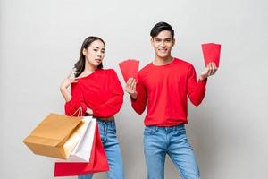 feliz casal asiático com sacolas de compras e envelopes vermelhos isolados em fundo de estúdio cinza para o conceito de venda de ano novo chinês