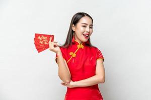 mulher asiática sorridente em traje oriental cheongsam segurando envelopes vermelhos ou ang pao isolado em fundo de estúdio cinza claro para conceitos de ano novo chinês, texto significa grande sorte grande lucro foto