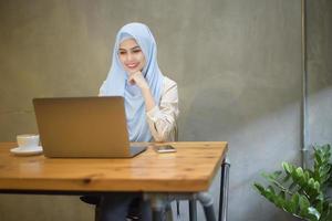 mulher muçulmana com hijab está trabalhando com computador portátil na cafeteria foto