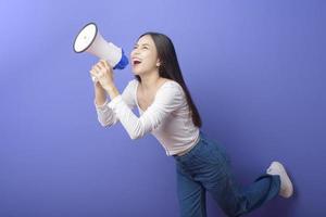 retrato de jovem e bela mulher sorridente está usando megafone para anunciar sobre estúdio de fundo roxo isolado foto