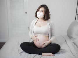 linda mulher grávida asiática está usando máscara protetora em sua casa, conceito de proteção contra coronavírus
