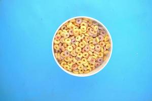 vista superior de flocos de milho de cereais coloridos em uma tigela sobre fundo azul foto