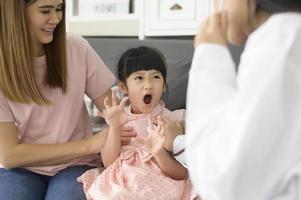 uma médica segurando estetoscópio está examinando uma garota feliz no hospital com sua mãe, conceito médico foto