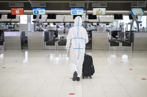 um homem asiático está vestindo traje de EPI no aeroporto internacional, viagens de segurança, proteção covid-19, conceito de distanciamento social foto