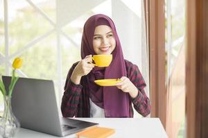 mulher muçulmana com hijab está trabalhando com computador portátil na cafeteria foto