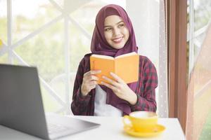 mulher muçulmana com hijab está trabalhando com computador portátil na cafeteria foto