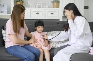 uma médica segurando estetoscópio está examinando uma garota feliz no hospital com sua mãe, conceito médico foto