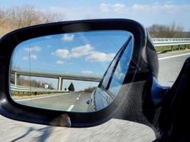 paisagem e reflexão da estrada no espelho retrovisor do carro preto. foto