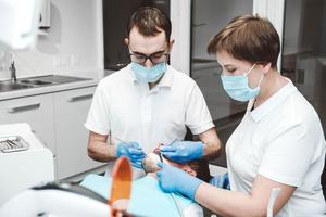 dentista e seu assistente tratam um paciente do sexo masculino em uma clínica odontológica. dentistas em máscaras médicas trabalhando com os dentes do cliente