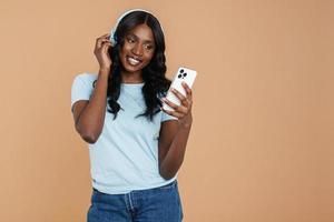 mulher africana sorridente, mensagens de texto por telefone com fones de ouvido foto