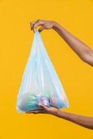 mãos femininas segurando um saco de lixo plástico azul com frutas