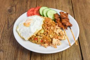 nasi goreng arroz frito frango com ovo tomate pepino na chapa branca e satay com molho - nasi goreng ayam comida indonésia asiática foto