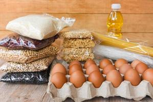 doações de alimentos com ovos arroz vários grãos de ervilha e alimentos secos óleo de cozinha não perecível macarrão instantâneo doar conceito no fundo da mesa de madeira foto