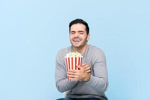 jovem segurando pipoca rindo enquanto assiste filme isolado em fundo azul claro foto