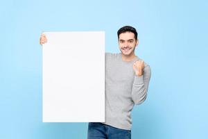 homem caucasiano bonito mostrando a placa de papel branco vazia com punho levantando sobre fundo isolado azul claro foto