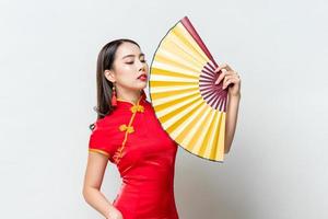 retrato de uma linda mulher asiática usando vestido vermelho tradicional qipao segurando leque dourado em estúdio isolado fundo cinza claro para o conceito de ano novo chinês foto