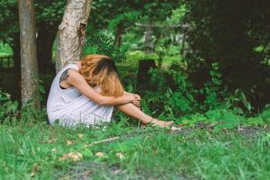 mulher jovem hippie, triste, cabelos compridos sentado abraçando as pernas. foto