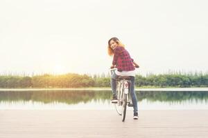 Bicicleta de pedal de pés de mulher na ponte de madeira, olhando para a câmera, relaxando a liberdade, pronta para andar de bicicleta. foto