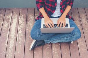 mãos de jovem hippie digitando laptop sentado no lago do cais, relaxando trabalhando ao ar livre. foto