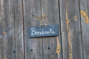 benvenuti é a tradução italiana da palavra inglesa boas-vindas pendurada em uma porta de madeira