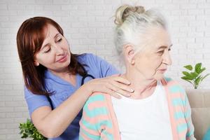 quiroprático feminino olhando para mulher sênior com dor no pescoço no consultório médico ou no quarto. Terapia Reabilitação do Idoso foto