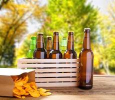 garrafas de cerveja e batatas fritas na mesa de madeira com parque turva no fundo, garrafa colorida, conceito de comida e bebida, foco seletivo, espaço de cópia foto